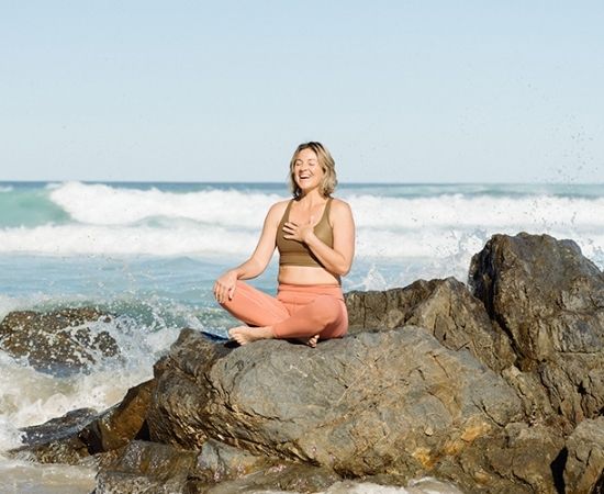 Woman sitting in sun on beach, smiling